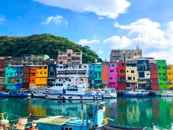 Sailboats moored on harbor by buildings against sky