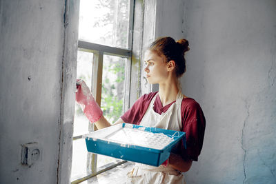 Young woman reading book while standing against wall