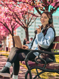 Young woman using mobile phone while sitting on bench in park