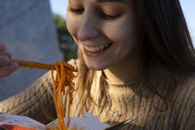 Young and beautiful girl eating some chinese noodles with chopsticks.