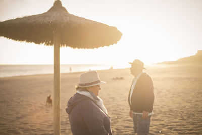 Senior people standing at beach against sky during sunset