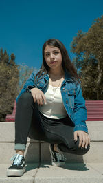 Portrait of young woman sitting on seat against clear sky