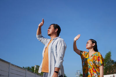 Low angle view of friends standing against clear blue sky