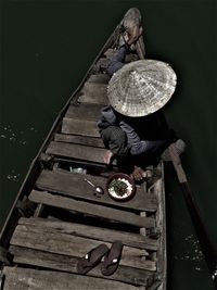 High angle view of man wearing asian style conical hat while sitting on wooden boat over river