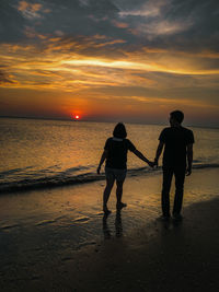 Silhouette people walking on beach against sky during sunset