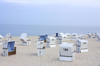 Tilt-shift image of hooded beach chairs with numbers on sand at beach against sky