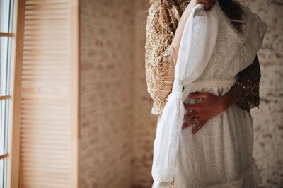 Midsection of woman holding wedding dress while standing against wall