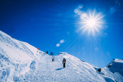 People skiing on snowcapped mountain against blue sky