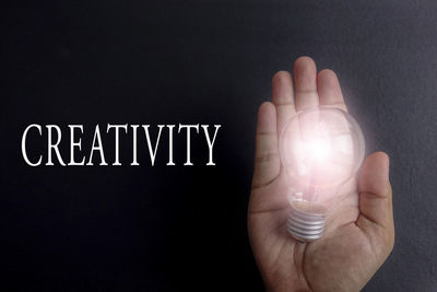 Close-up of hand holding light bulb over black background