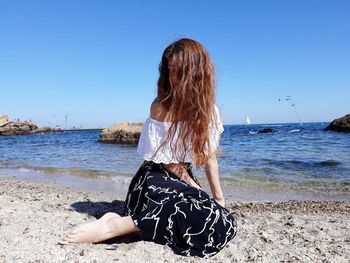 Rear view of woman at beach against clear sky