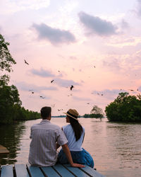 Rear view of man sitting on pier against lake during sunset