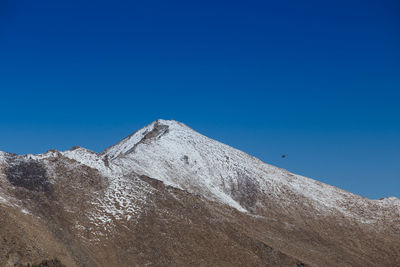 Low angle view of snowcapped mountain against clear blue sky