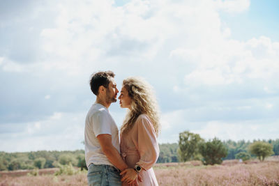 Side view of couple standing on field against sky and looking to each other