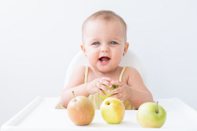 Portrait of cute boy holding apple on table against white background