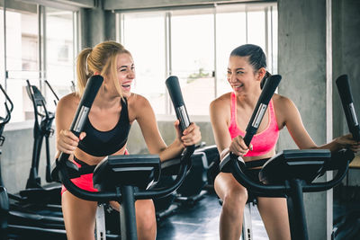 Happy young women on exercise bikes at gym