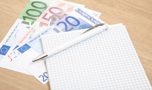 High angle view of pen and book euro banknotes on table