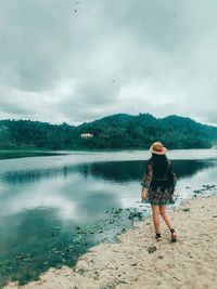 Full length of woman walking at lakeshore against cloudy sky