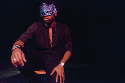 Portrait of young man sitting against black background