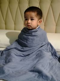 Cute baby boy wrapped in blanket on bed at home