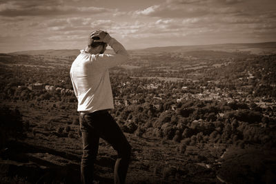 Rear view of man standing on mountain looking at landscape against sky