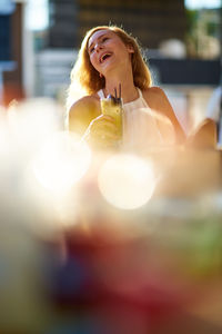 Smiling young woman having drink in sunny day