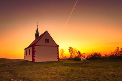 Building on field against sky during sunset