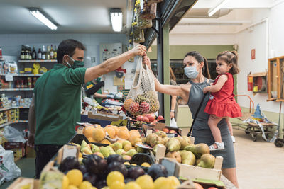 A young woman with a mask shopping at the fruit shop with her daughter