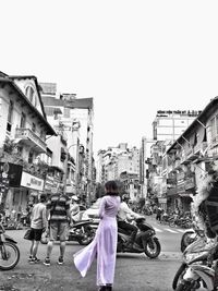 Woman riding bicycle on street in city against clear sky