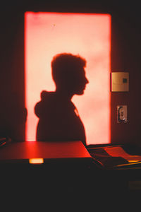 Rear view of silhouette boy sitting on table at home