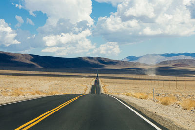 Empty desert road towards mountains against sky