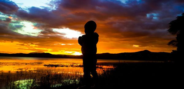 Silhouette man standing by lake against sky during sunset