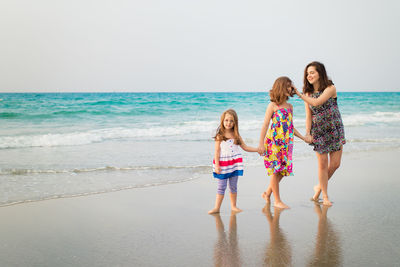 Happy friends standing on beach against sea