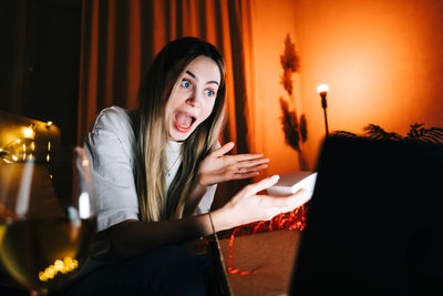 Surprised woman holding gift doing video call on laptop at home