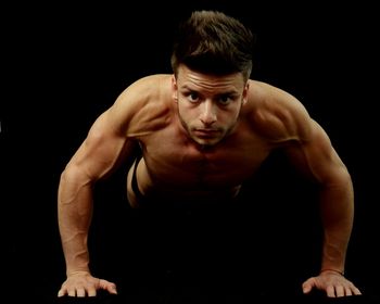 Portrait of shirtless muscular man exercising against black background