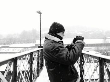 Mature man photographing while standing on footbridge during winter