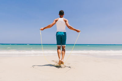 Full length of man exercising at beach against clear sky