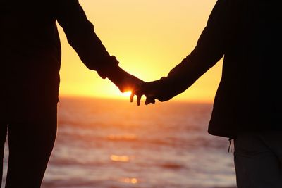 Silhouette couple holding hands at beach during sunset