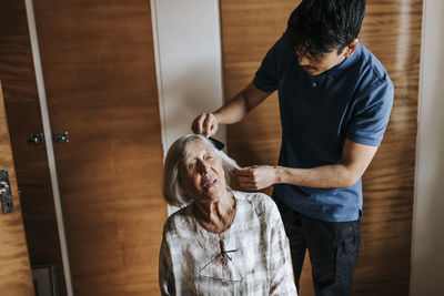 Male care assistant combing hair of senior woman at home