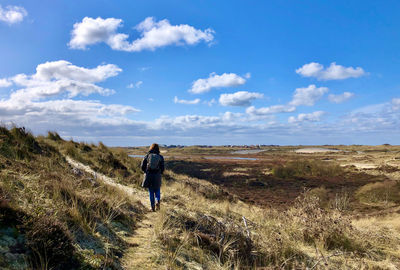 Rear view of man walking on field against sky