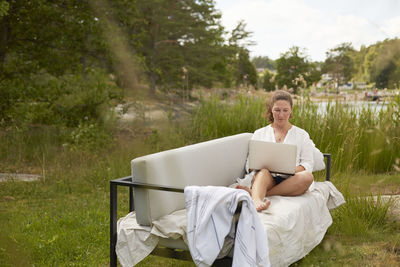 Woman using laptop on garden bench barefoot