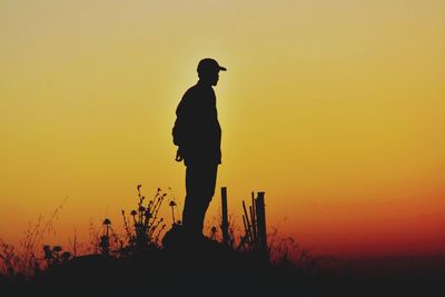 Silhouette man standing by plants against orange sky