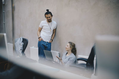 Computer programmers discussing over laptop against wall in office