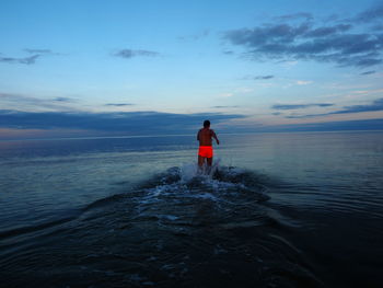 Rear view of man on sea against sky during sunset