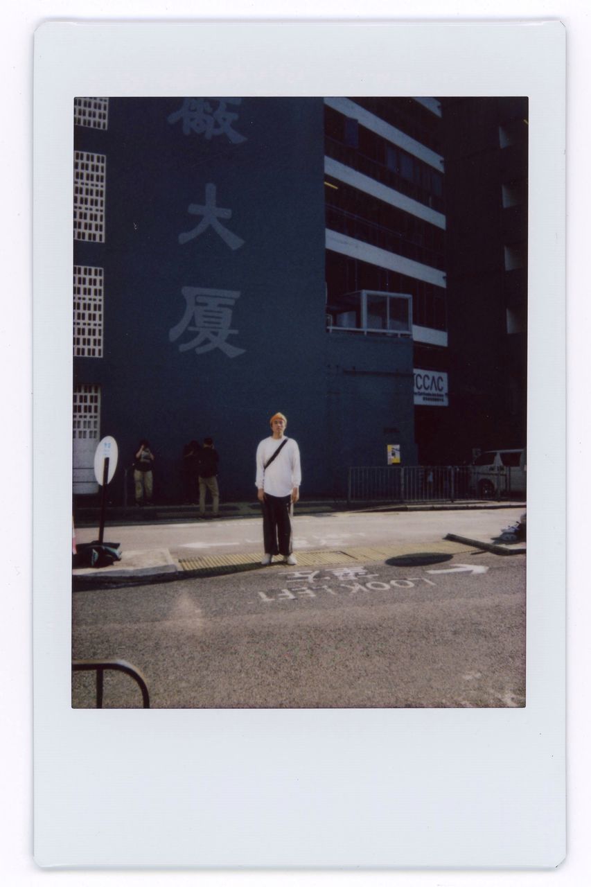 REAR VIEW OF MAN STANDING BY BUILDING