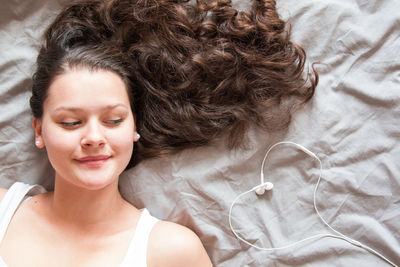 Directly above shot of woman looking at heart shape made with in-ear headphones on bed