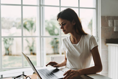 Woman looking at camera while sitting on window