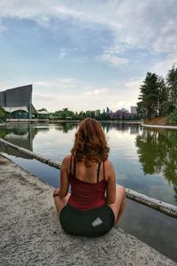 Rear view of woman sitting on riverbank against sky