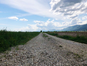 Empty road amidst field against sky