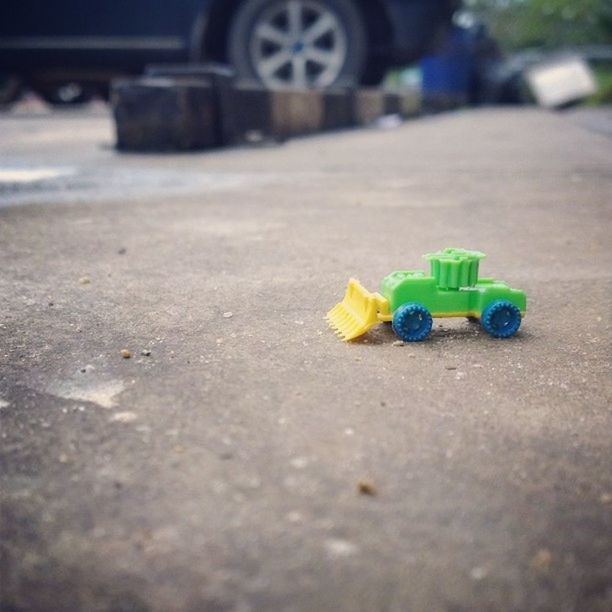 selective focus, toy, street, multi colored, childhood, still life, close-up, road, surface level, focus on foreground, high angle view, yellow, guidance, asphalt, day, no people, plastic, art and craft, outdoors, single object
