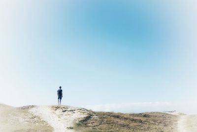 Rear view of man standing on sand dune against sky